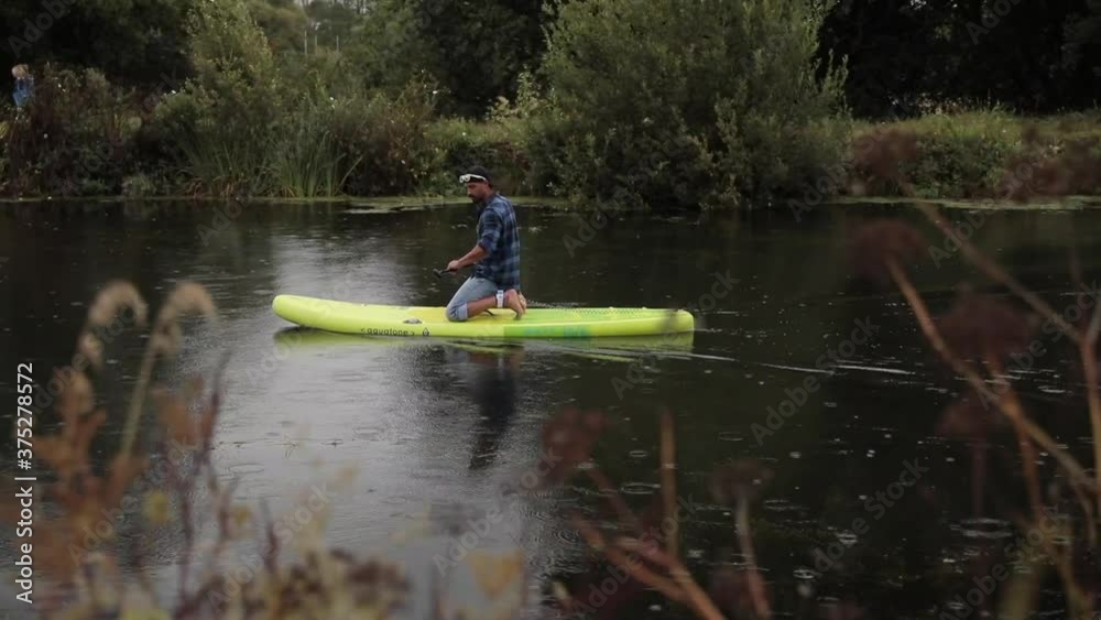 A tracking shot of a paddleboarder working his was upstream on his knees A tracking shot of a paddleboarder working his was upstream on his knees