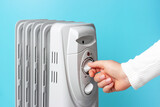 The girl turns on the heater on blue background, side view