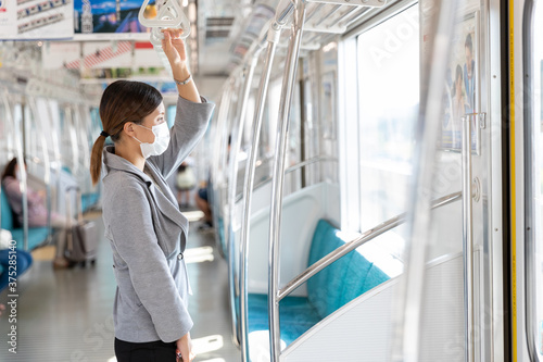 マスク姿でつり革に掴まって電車通勤をする女性