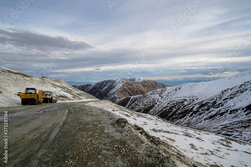 A yellow tractor on a deserted road covered with snow surrounded in South Island, New zealand.