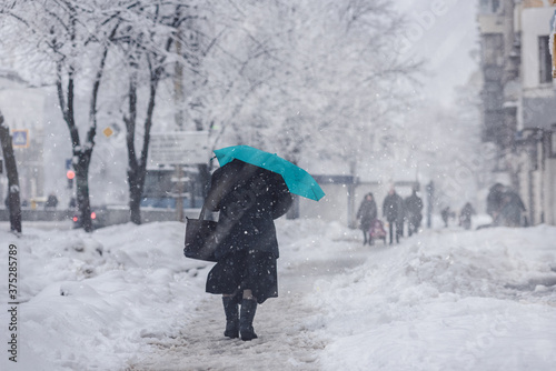 Woman in wet shoes and coat with umbrella walking on street during blizzard
