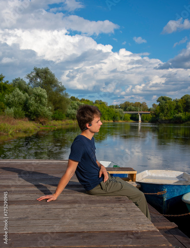 A young man sits on a boat dock on a bright summer day.