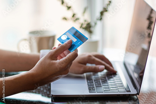 Young woman holding credit card and using laptop computer. Online shopping, e-commerce, internet banking, spending money, working from home concept