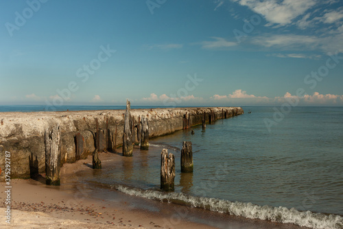 a decaying old concrete breakwater, rusty parts of the structure, old wooden piles stuck in the shore