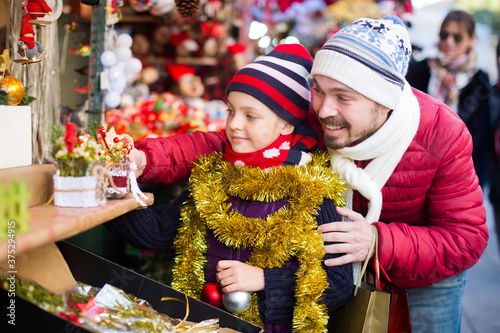 Adult man with small daughter near the customer counter with Christmas garlands