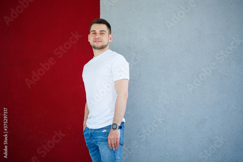 Stylish young man, a man dressed in a white blank t-shirt standing on a gray and red wall background. Urban style of clothes, modern fashionable image. Men's fashion