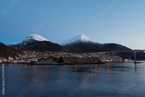 The city Maloy in Norway seen from cruise ship in early morning with snow capped mountains on clear winter day
