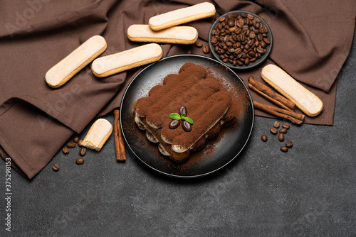 Classic tiramisu dessert on ceramic plate and savoiardi cookies on concrete background