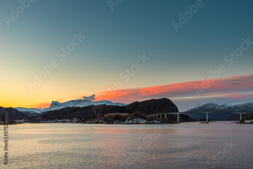 Colorful dawn over the coastline of Norway near the town Maloy with bridge, hills and snow capped mountains seen from cruise ship photo