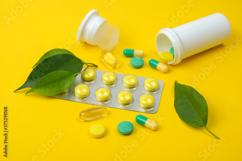 Yellow and green pills, jar and green leaves on a yellow background.