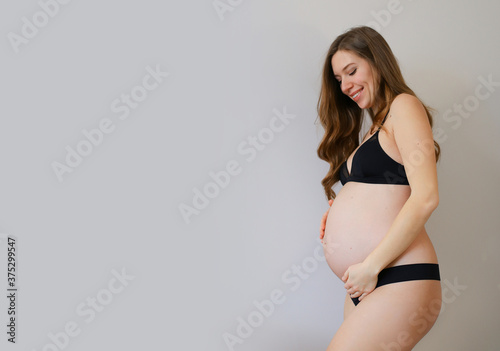 Busty pregnant woman in trendy gray underwear hugs her belly. A