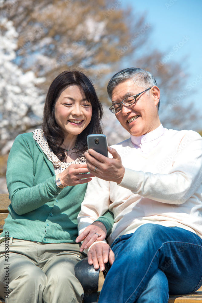 Fototapeta premium ベンチに座りスマートフォンを見るミドル夫婦