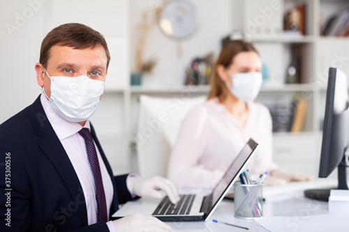 Focused businessman in disposable face mask and rubber gloves working with female assistant in office. Necessary precautions during COVID 19 pandemic..