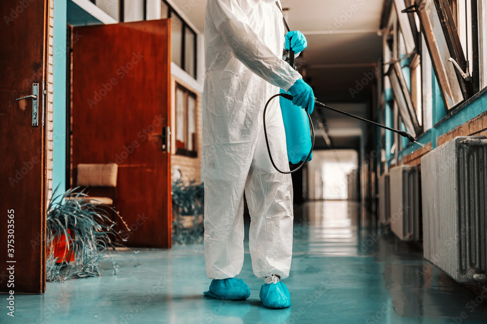 Worker in sterile uniform, with rubber gloves holding sprayer with
