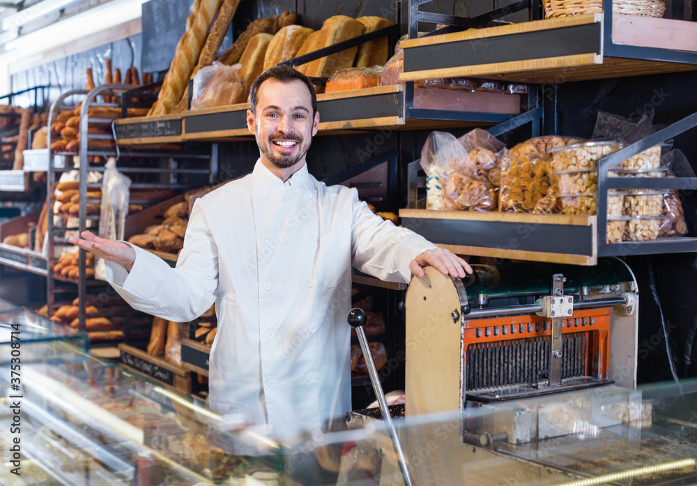 Young cheerful man seller displaying assortment of bakery