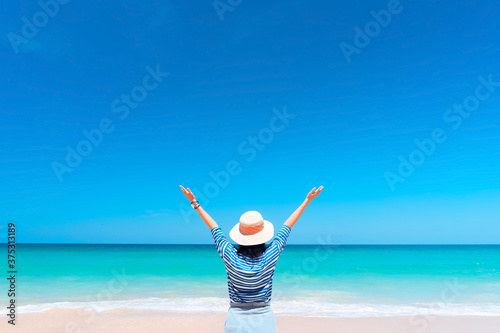 Happy woman raise hand up at tropical beach with blue sky background. Travel vacation and freedom feel good concept.