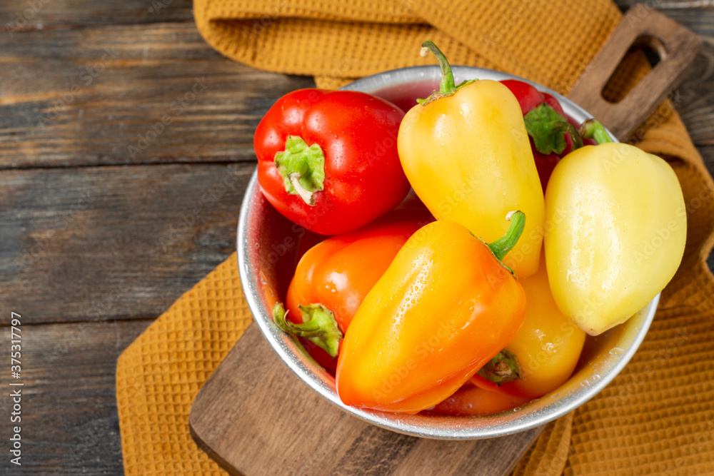 Sweet pepper. Red and yellow and orange peppers in a metal bowl on a brown wooden table. Pepper close-up Sweet pepper. Red and yellow and orange peppers in a metal bowl on a brown wooden table. Pepper close-up
