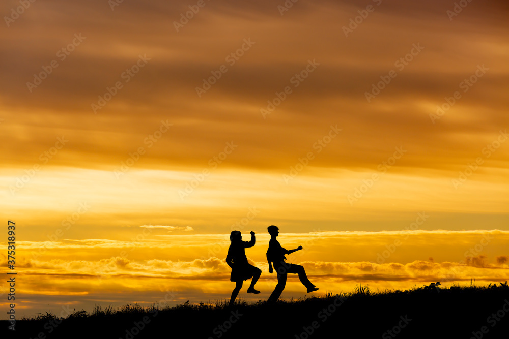 夕陽を背景に元気よく歩く男女高校生のシルエット