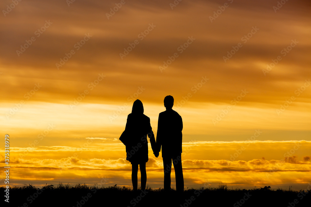 夕陽を背景に手をつなぎ立つ男女のシルエット