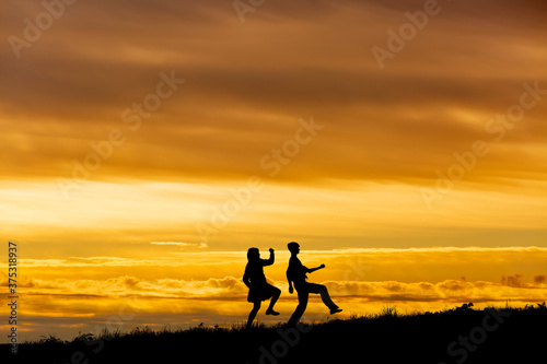 夕陽を背景に元気よく歩く男女高校生のシルエット