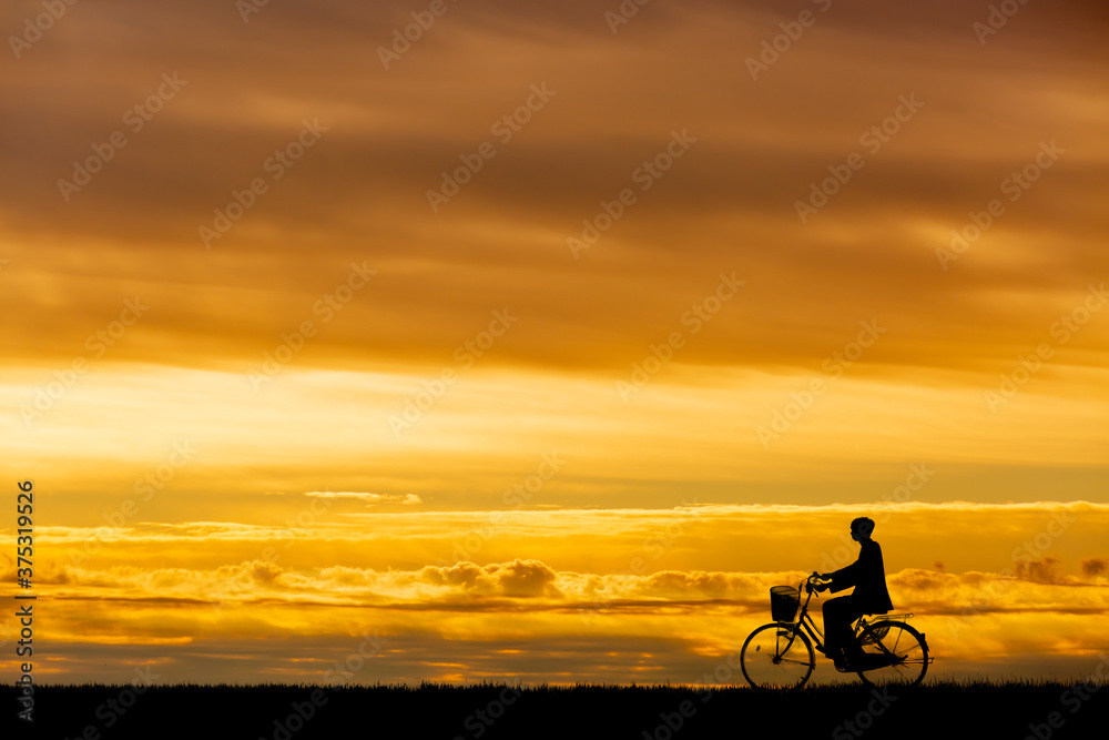 Fototapeta premium 夕陽を背景に自転車通学する男子高校生のシルエット