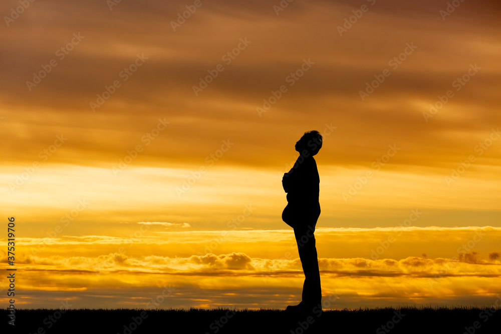 夕陽を背景に腕組みし立つ男性の横姿シルエット