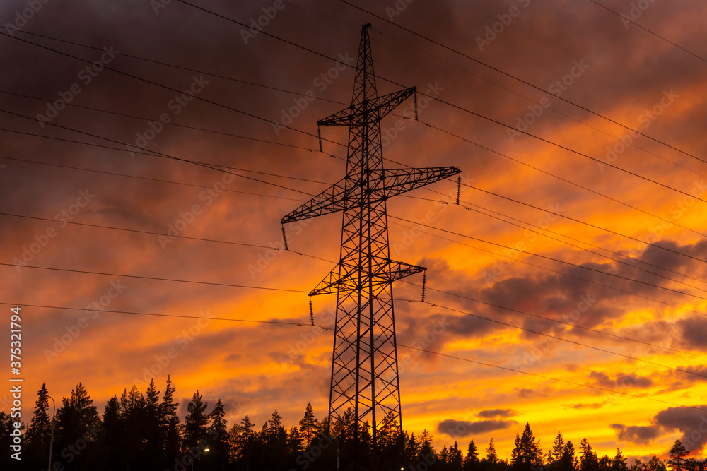 Silhouette of mast with electric cables sunset sky on background with fire smoke