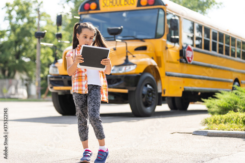 adorable little schoolgirl near school bus and looking at camera