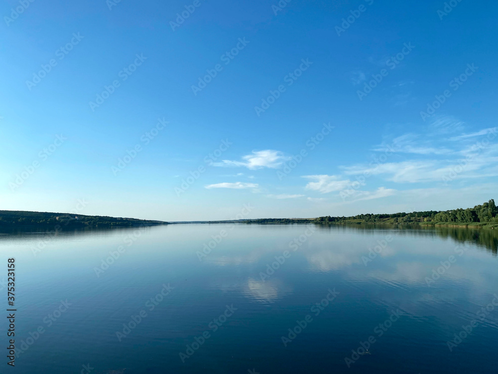 Landscape . Reflection of a blue sky with white clouds in a lake. A view of the horizon near the river in a summer evening. Mobile photography, horizontal.