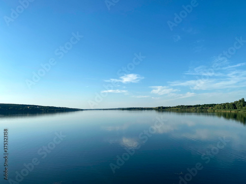 Landscape . Reflection of a blue sky with white clouds in a lake. A view of the horizon near the river in a summer evening. Mobile photography  horizontal.