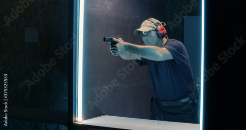 Photos Mature shooter firing pistol in dark range