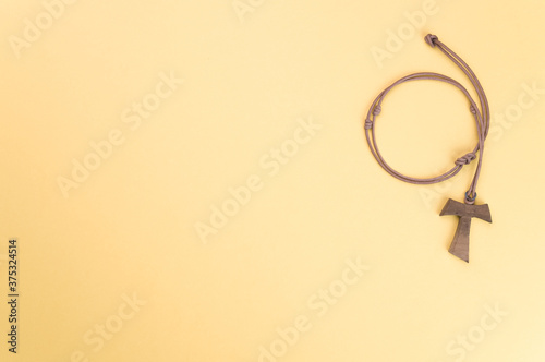 Closeup of a wooden tau cross necklace isolated on a yellow background