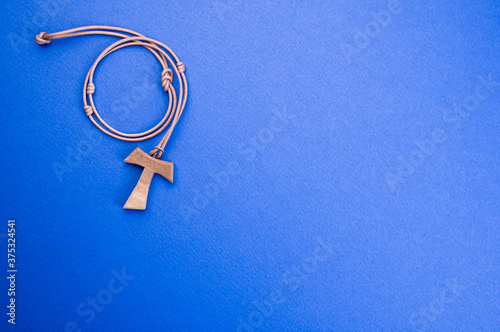 Closeup of a wooden tau cross necklace isolated on a blue background