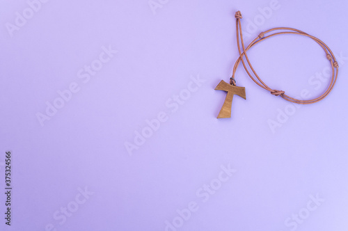 Closeup of a wooden tau cross necklace isolated on a purple background