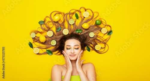 peaceful girl lying on yellow background with citrus fruits in long hair young woman head with lemon slices and leaves  concept of female beauty