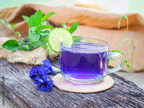 Fresh purple Butterfly pea or blue pea flower and juice in glass with lime on wooden table. 