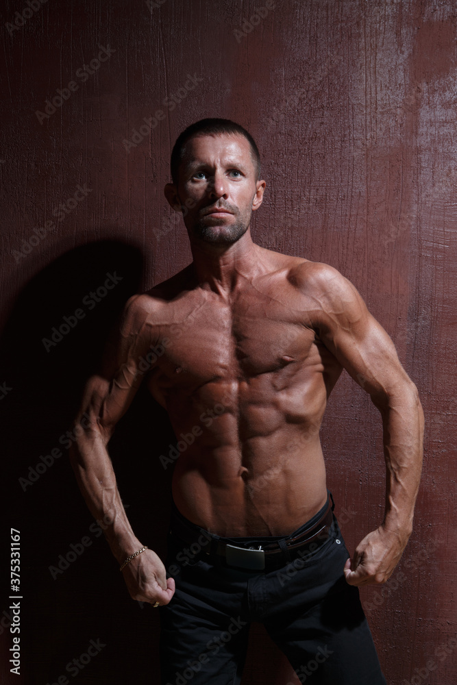 A slender, athletic man with a naked muscular torso on a dark background.