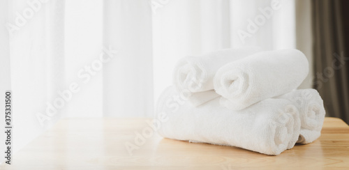 White soft towels folded on wood table with blurred white bathroom background