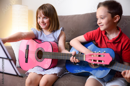 Girl and boy practicing guitar sitting on sofa at home photo