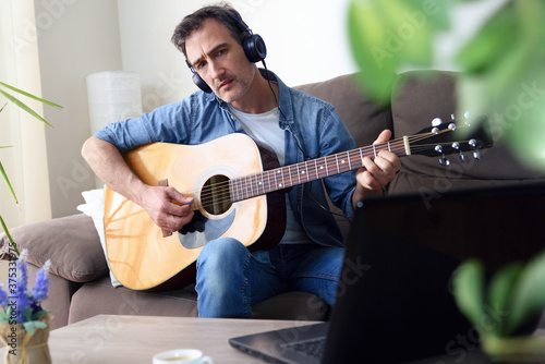 Man playing guitar and listening and looking at a laptop