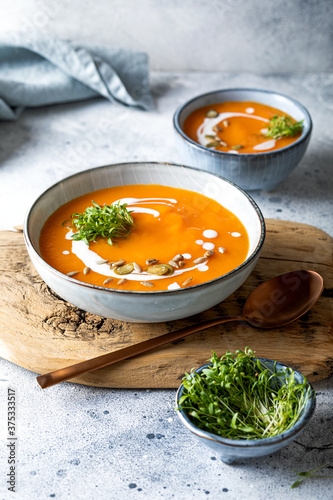 Vegetarian autumn pumpkin and carrot soup with cream, seeds and cilantro micro greens. Comfort food, fall and winter healthy slow food concept