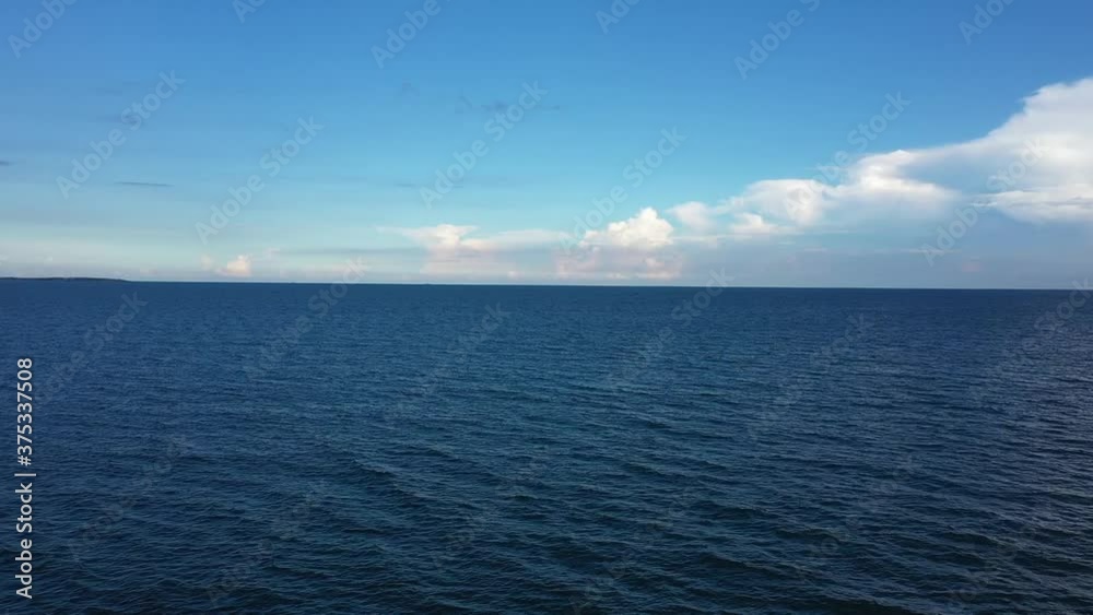 Aerial view to blue sea and magic sunset clouds. Move straight, go along the horizon. Surfer's silhouette on dark ocean and puffy clouds on blue sky. Calm sea waves with pearl clouds in distance Aerial view to blue sea and magic sunset clouds. Move straight, go along the horizon. Surfer's silhouette on dark ocean and puffy clouds on blue sky. Calm sea waves with pearl clouds in distance