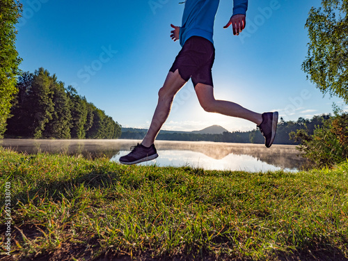 Athlete runner running on gras at summer lake