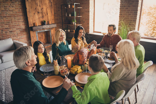 Photo of full family eight members gathering sit two little kids hold hands eyes closed pray thank god rich harvest dishes dinner table multi-generation in evening living room indoors