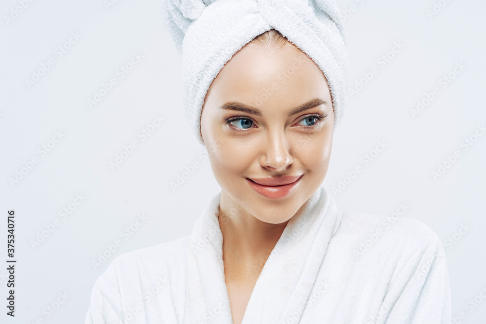 Day spa, beauty and freshness concept. Pensive European woman with healthy skin concentrated aside thoughtfully, feels refreshed after bath procedures, dressed in dressing gown, towel on head Day spa, beauty and freshness concept. Pensive European woman with healthy skin concentrated aside thoughtfully, feels refreshed after bath procedures, dressed in dressing gown, towel on head