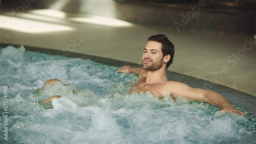 Attractive man resting whirlpool bath indoor. Happy man relaxing in pool.