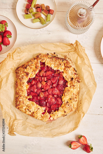 High angle shot of delicious rhubarb strawberries gallate cake with ingredients on a white table photo