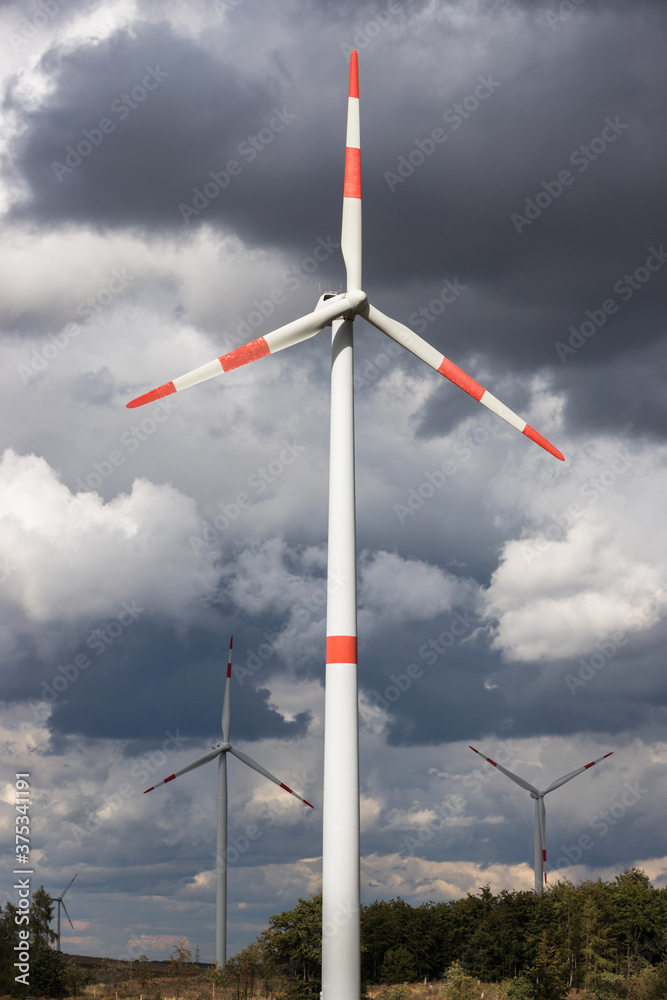 modern wind wheels in front of a cloudy storm sky landscape perpendicular