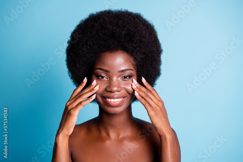 Closeup portrait photo of dark skin big volume wavy hairstyle lovely cute woman hands cheekbones applying cream beaming smiling well-being concept naked isolated blue color background