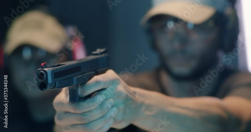 Focused male shooter firing pistol near instructor photo